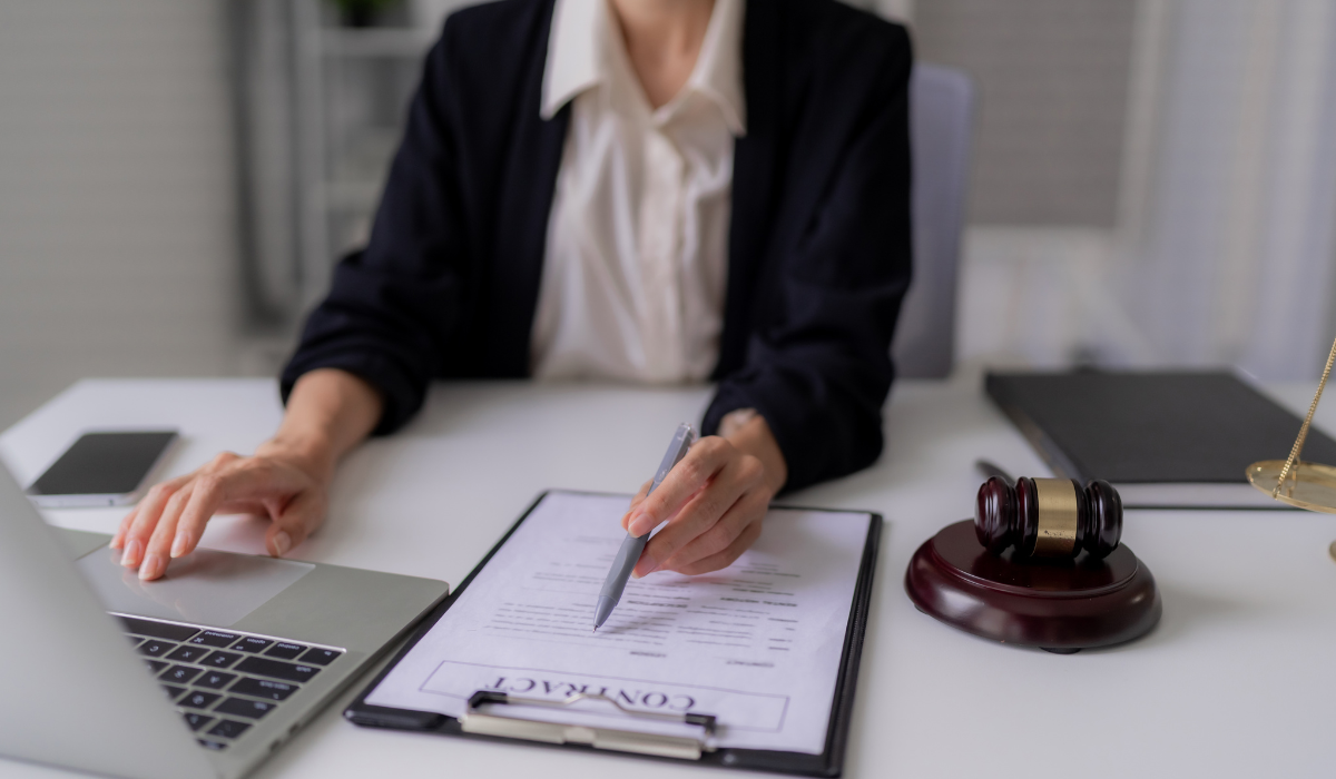 A woman in business attire sits at a desk and examines a legal document with an open laptop next to her, working to ensure secure legal document translation and legal document security.